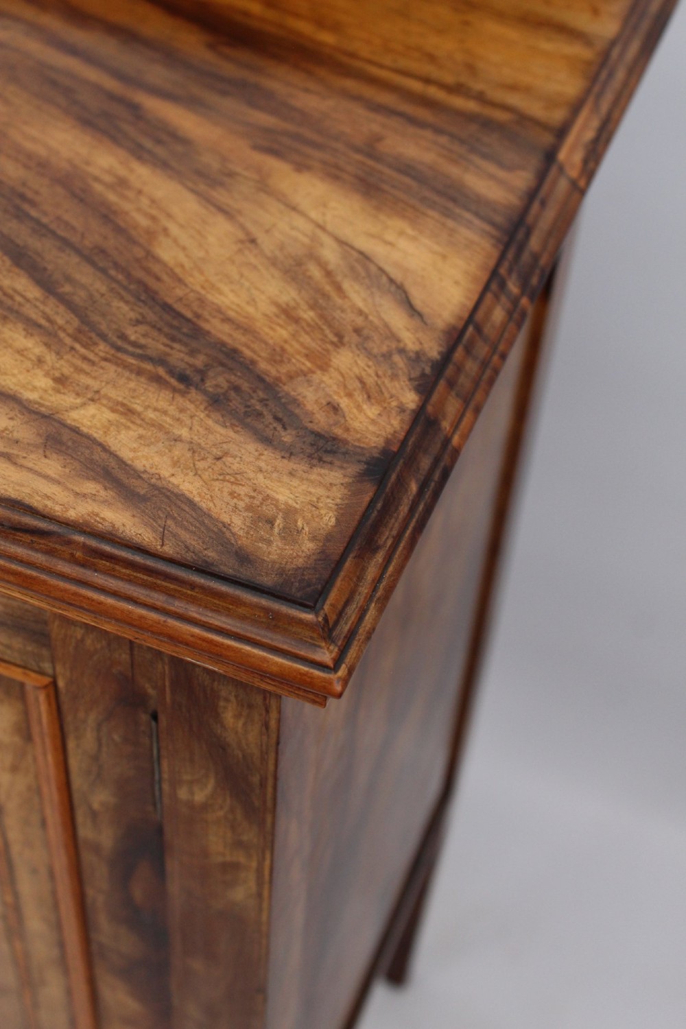 An Edwardian burr walnut bedside cabinet featuring a small gallery top, crossbanded inlaid door panel, drop brass handle, and square tapered legs. View XI