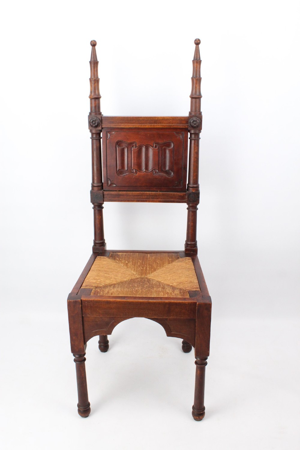 A Victorian Gothic Revival side chair made of dark oak with turned finials, a carved rectangular back panel, pointed arch aprons, and a woven rush seat. View II