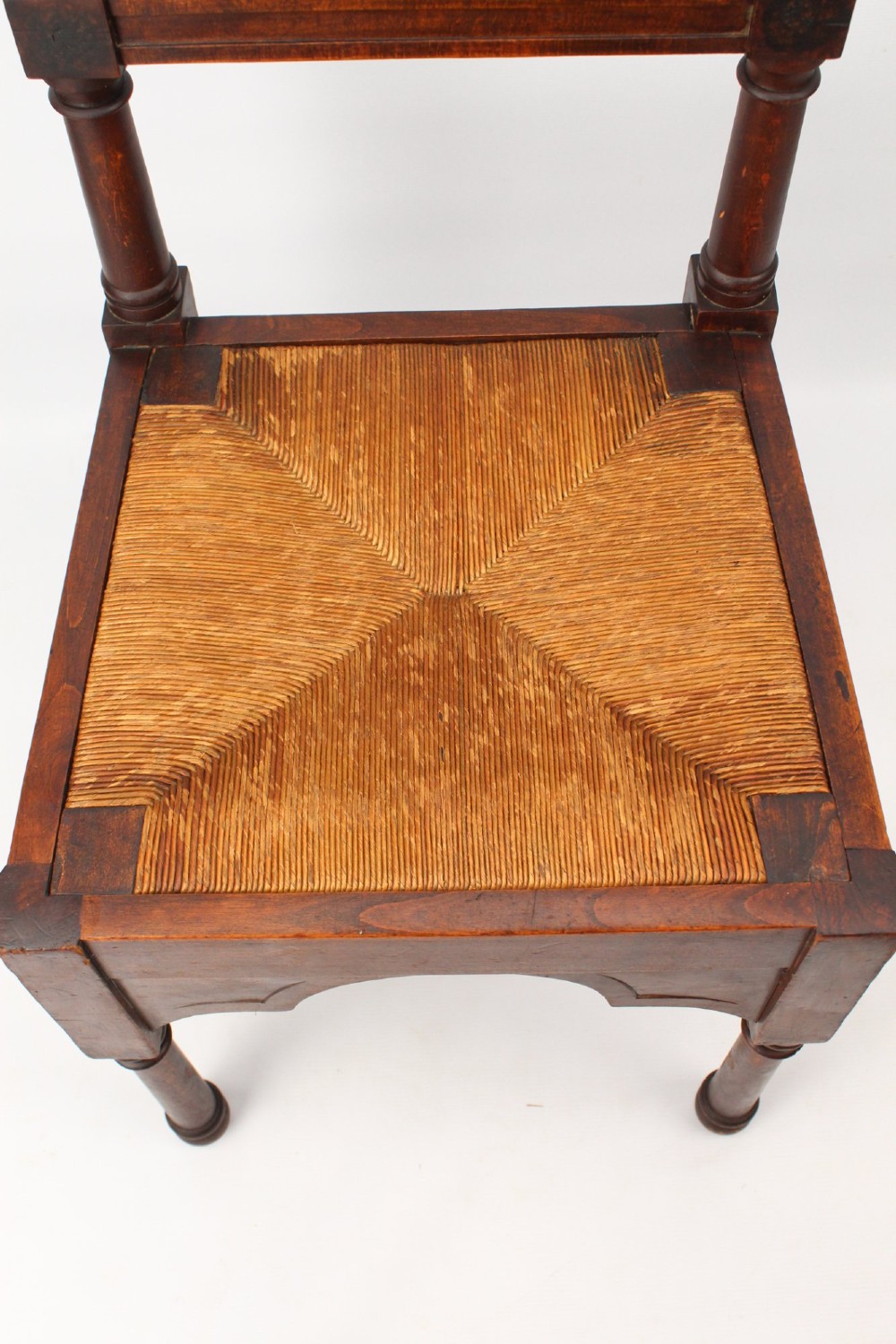 A Victorian Gothic Revival side chair made of dark oak with turned finials, a carved rectangular back panel, pointed arch aprons, and a woven rush seat. View VI