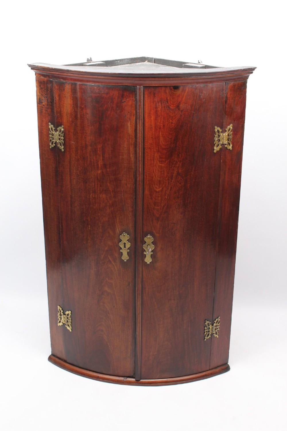A Georgian mahogany bow front corner cupboard with twin curved doors and decorative brass hinges and keyhole escutcheons. View II