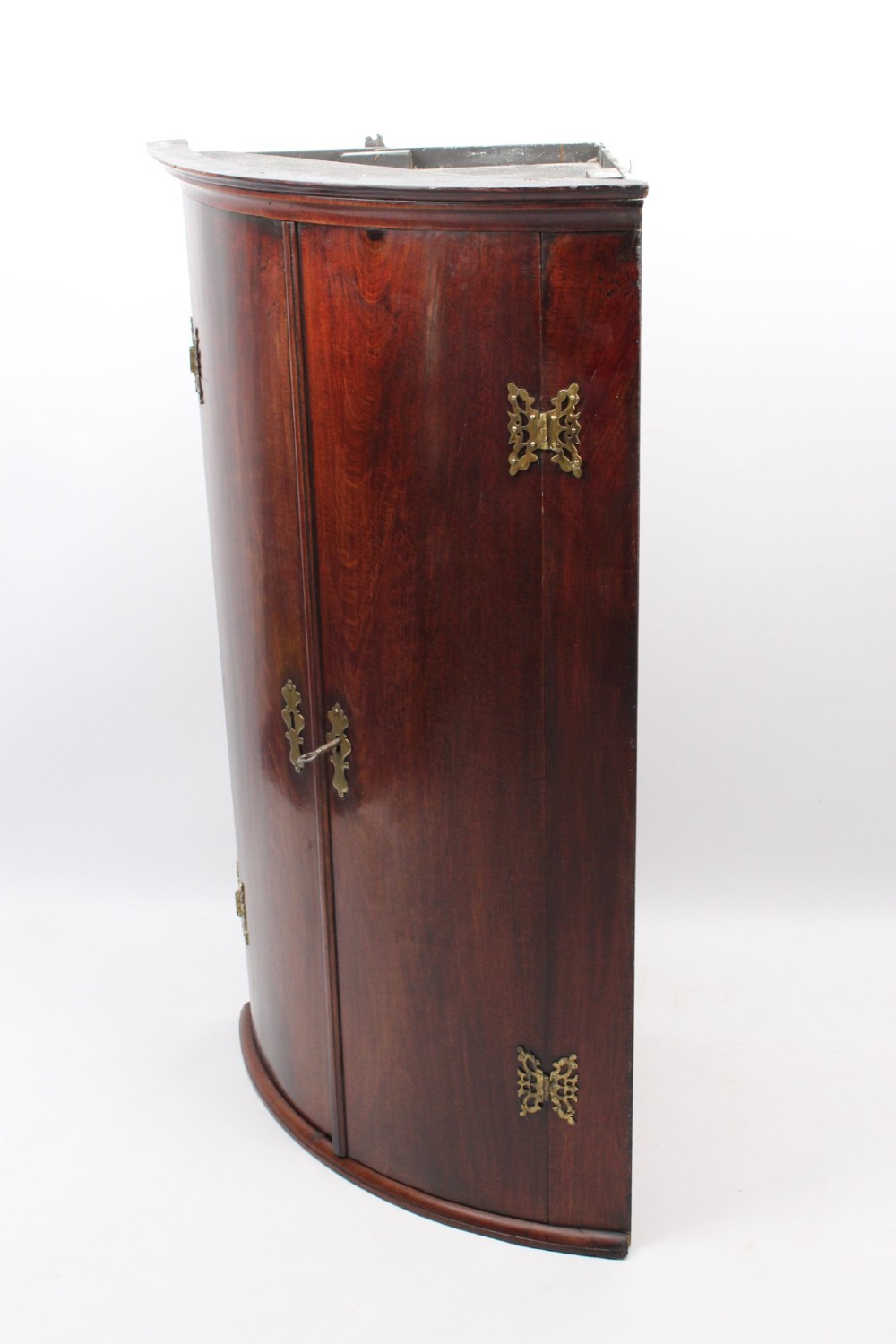 A Georgian mahogany bow front corner cupboard with twin curved doors and decorative brass hinges and keyhole escutcheons. View V