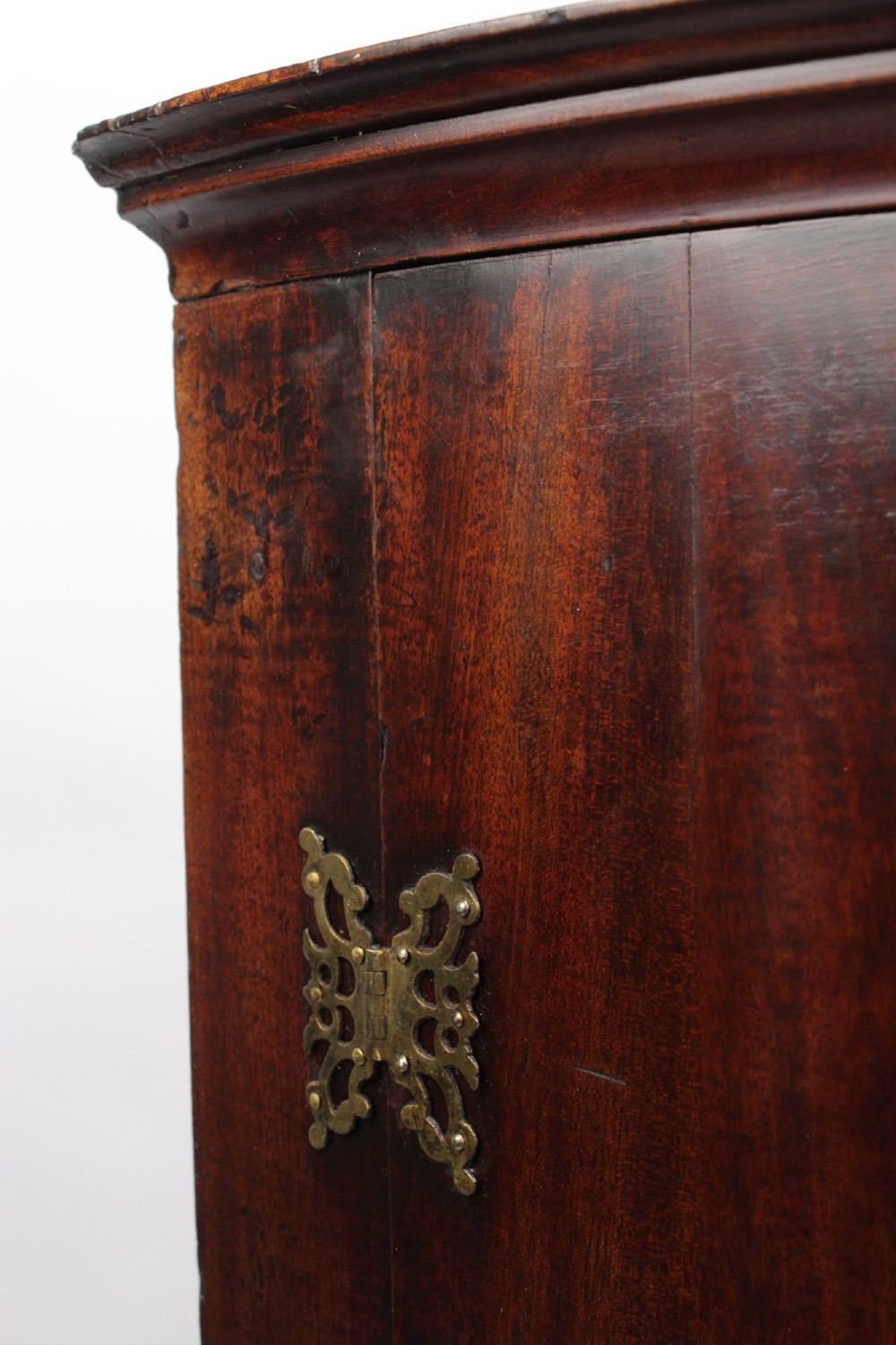 A Georgian mahogany bow front corner cupboard with twin curved doors and decorative brass hinges and keyhole escutcheons. View X