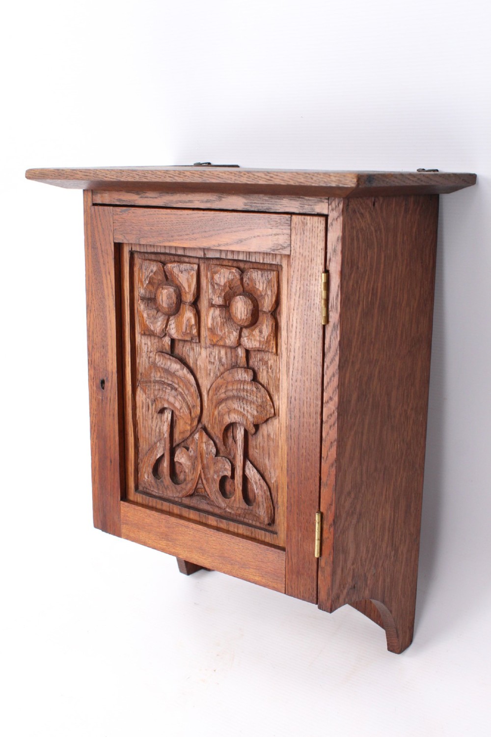 A small Edwardian Arts and Crafts oak wall cabinet featuring a single door decorated with a carved stylized floral panel and small brass hinges. View III