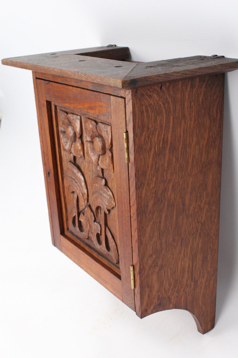 A small Edwardian Arts and Crafts oak wall cabinet featuring a single door decorated with a carved stylized floral panel and small brass hinges. View IV