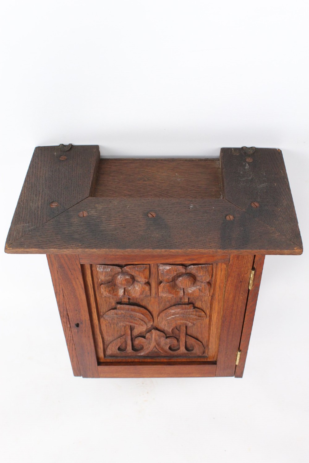 A small Edwardian Arts and Crafts oak wall cabinet featuring a single door decorated with a carved stylized floral panel and small brass hinges. View V