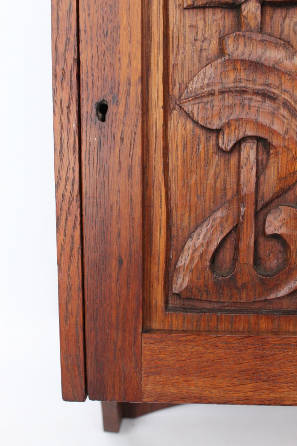 A small Edwardian Arts and Crafts oak wall cabinet featuring a single door decorated with a carved stylized floral panel and small brass hinges. View VI