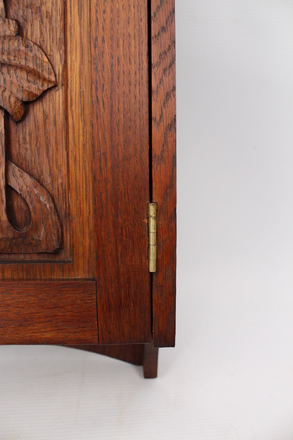 A small Edwardian Arts and Crafts oak wall cabinet featuring a single door decorated with a carved stylized floral panel and small brass hinges. View IX