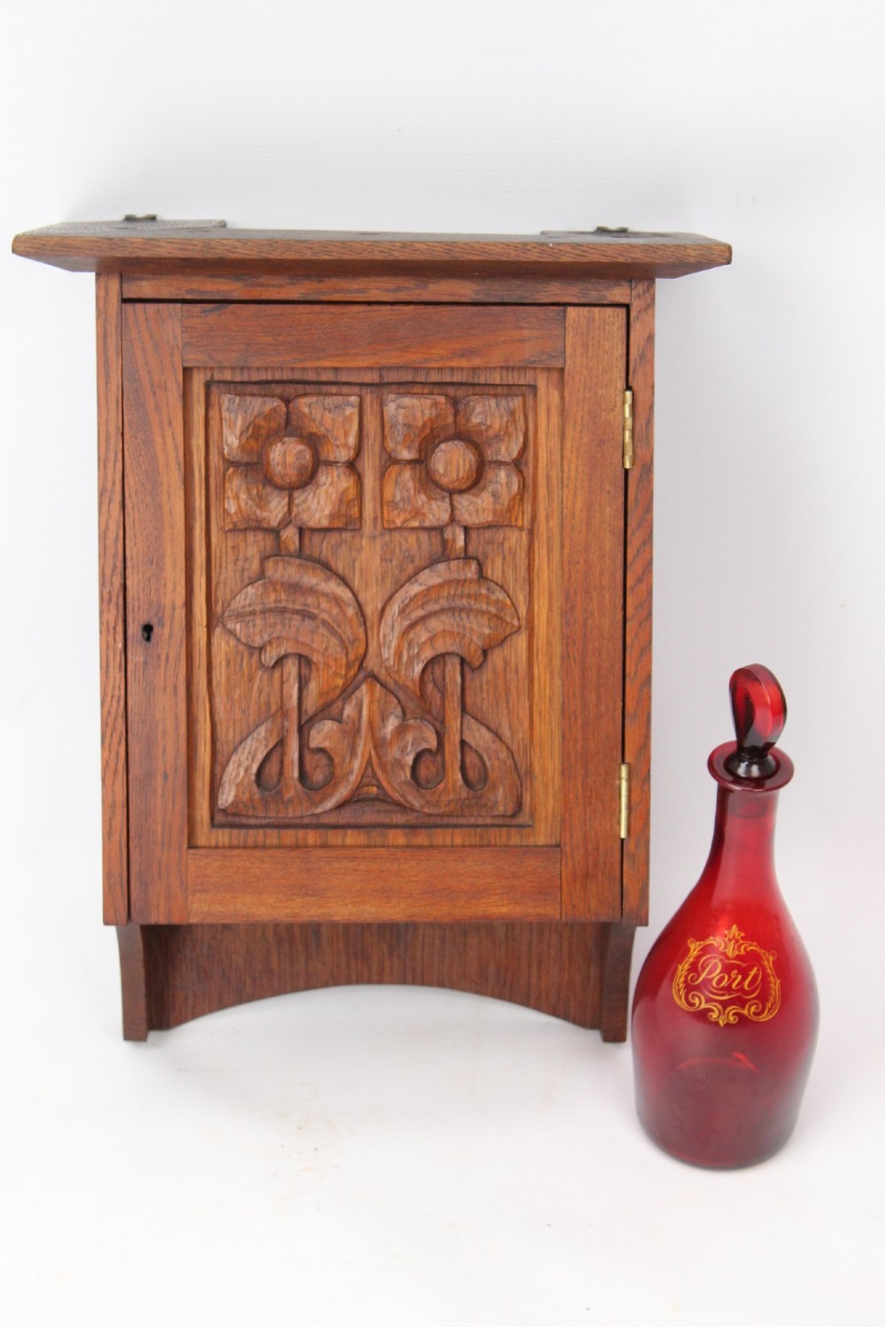 A small Edwardian Arts and Crafts oak wall cabinet featuring a single door decorated with a carved stylized floral panel and small brass hinges. View XII