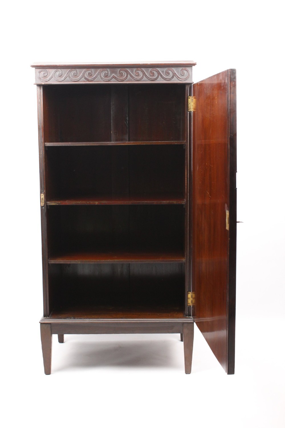 An Edwardian dark mahogany pedestal cabinet featuring an oval flame mahogany panel, carved scroll frieze, and square tapered legs. View II