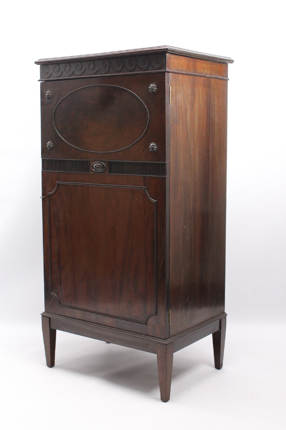 An Edwardian dark mahogany pedestal cabinet featuring an oval flame mahogany panel, carved scroll frieze, and square tapered legs. View III