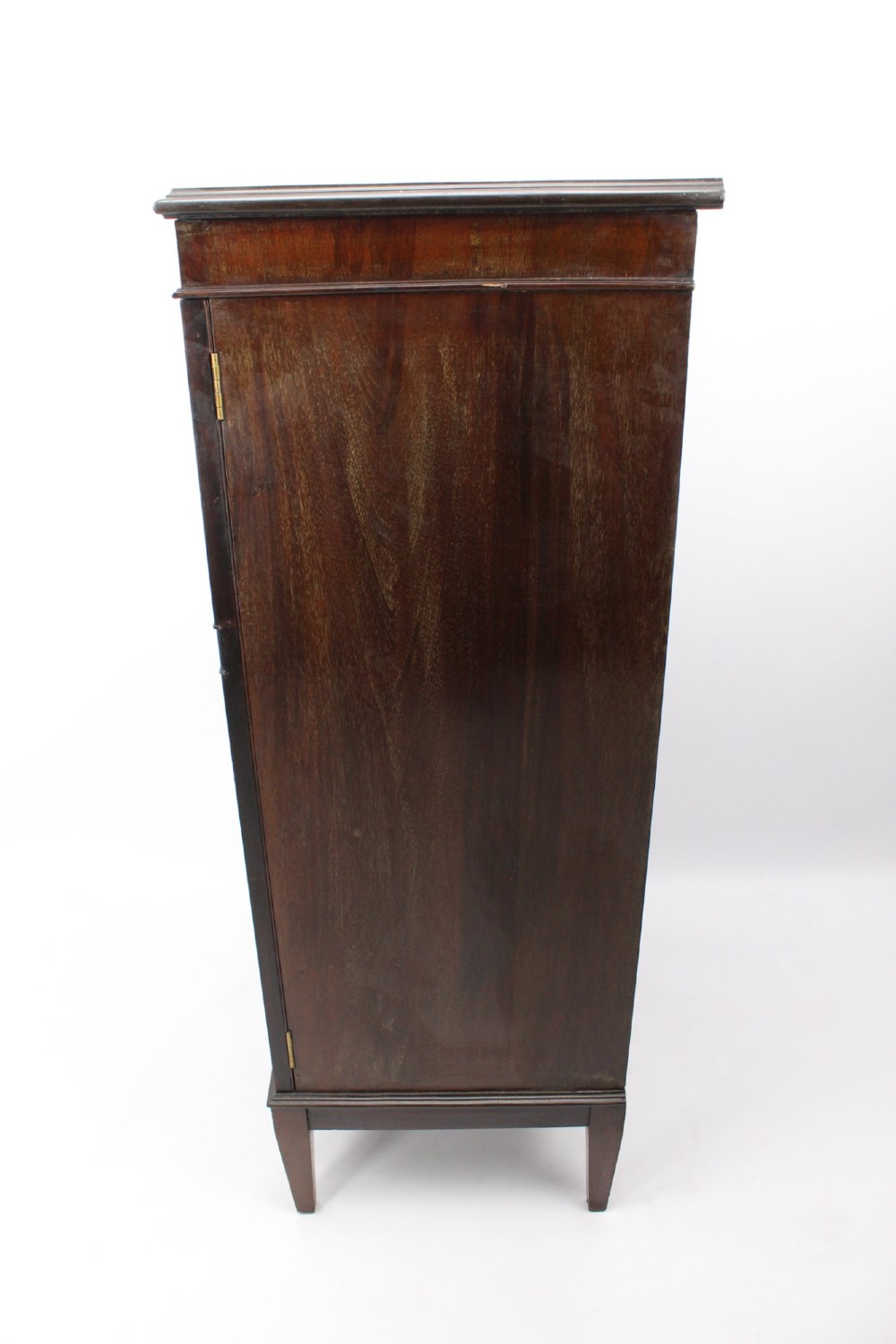 An Edwardian dark mahogany pedestal cabinet featuring an oval flame mahogany panel, carved scroll frieze, and square tapered legs. View V