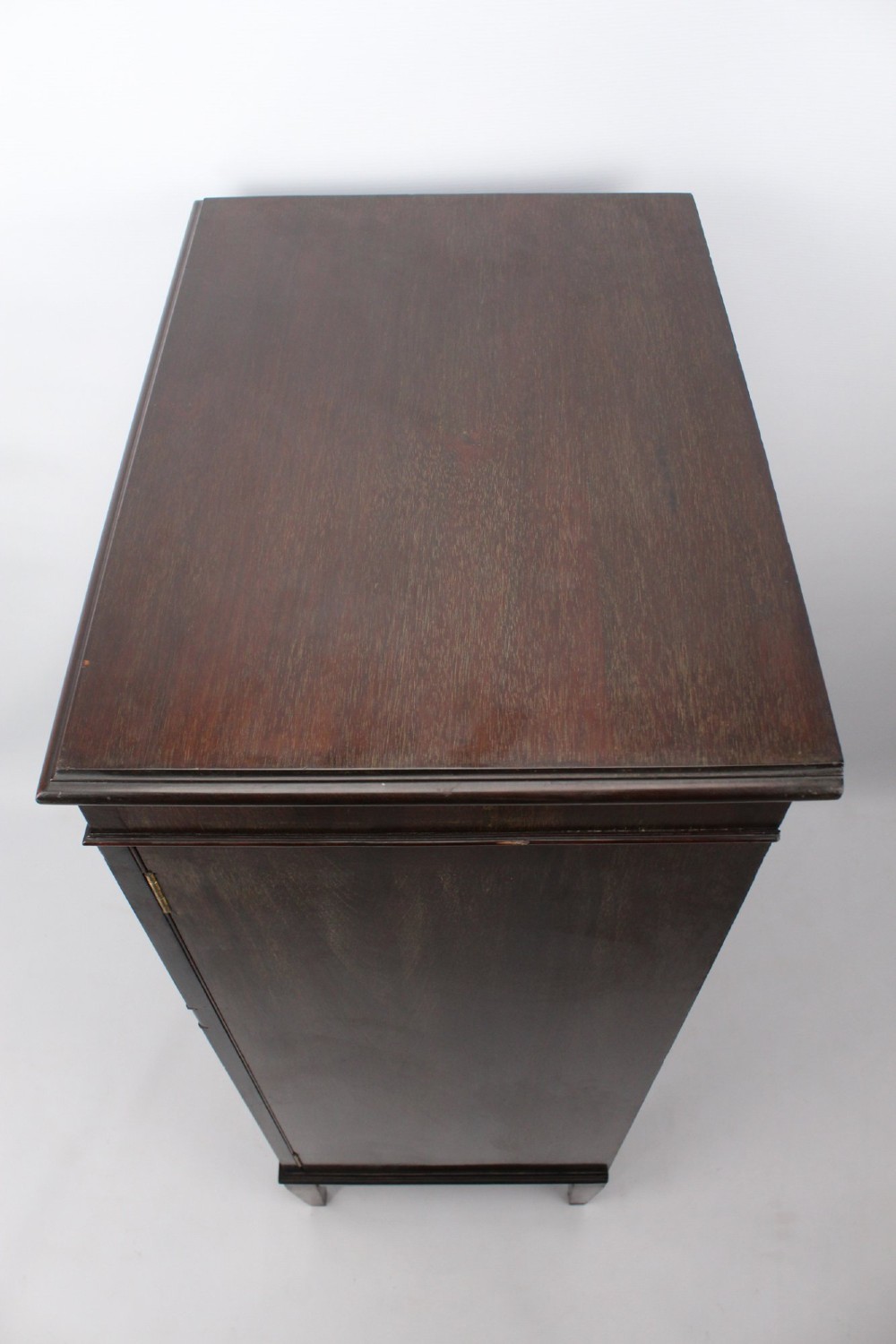 An Edwardian dark mahogany pedestal cabinet featuring an oval flame mahogany panel, carved scroll frieze, and square tapered legs. View VIII