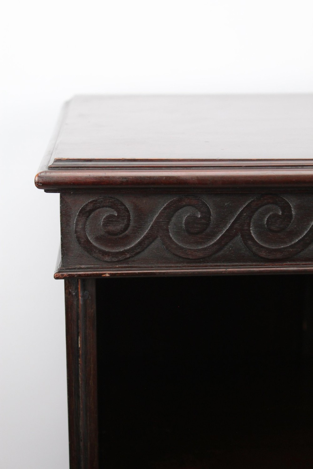 An Edwardian dark mahogany pedestal cabinet featuring an oval flame mahogany panel, carved scroll frieze, and square tapered legs. View IX