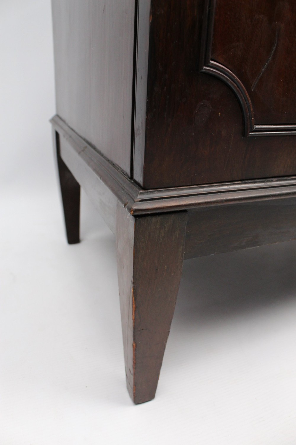 An Edwardian dark mahogany pedestal cabinet featuring an oval flame mahogany panel, carved scroll frieze, and square tapered legs. View XII
