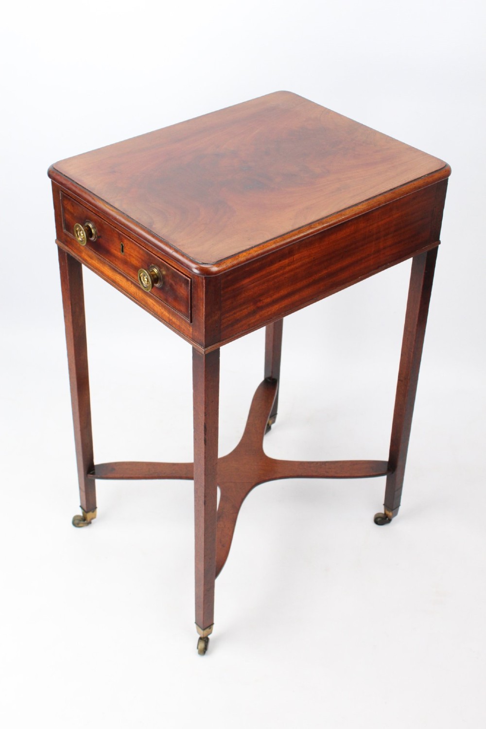A small Georgian mahogany side table featuring a single drawer with brass ring handles, square tapered legs joined by an X-form stretcher, and brass castors.
