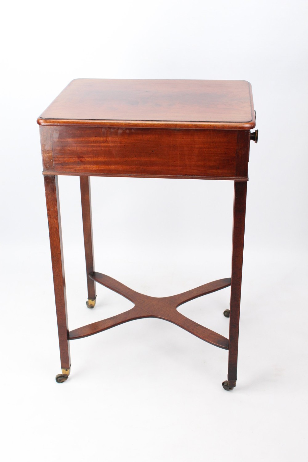 A small Georgian mahogany side table featuring a single drawer with brass ring handles, square tapered legs joined by an X-form stretcher, and brass castors. View IV
