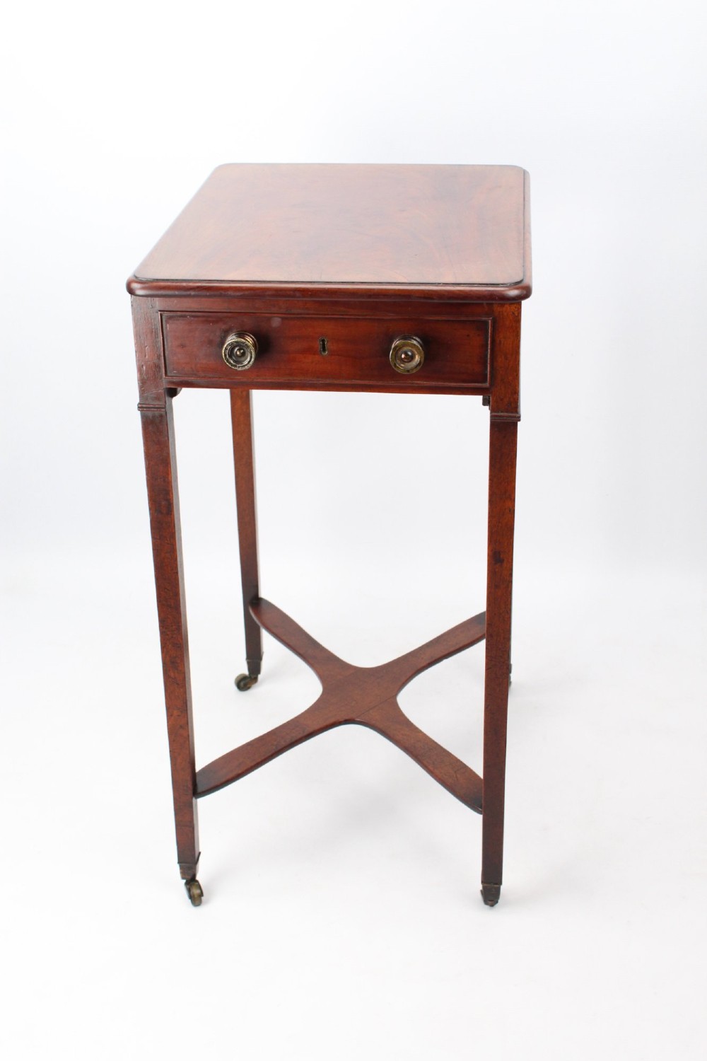 A small Georgian mahogany side table featuring a single drawer with brass ring handles, square tapered legs joined by an X-form stretcher, and brass castors. View V