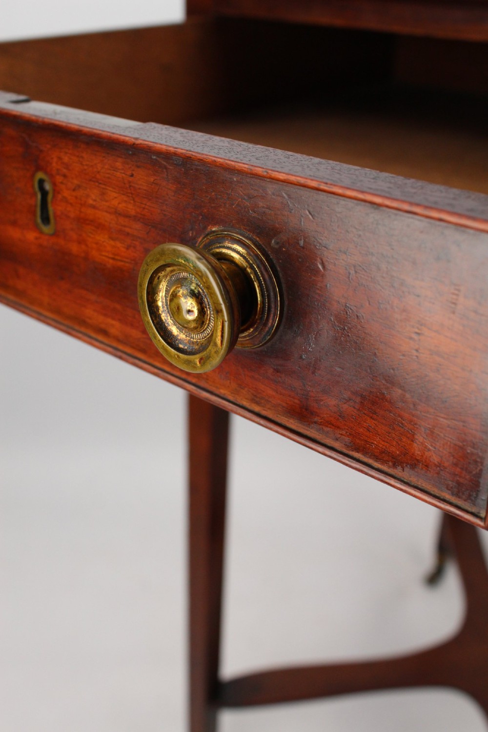 A small Georgian mahogany side table featuring a single drawer with brass ring handles, square tapered legs joined by an X-form stretcher, and brass castors. View VII