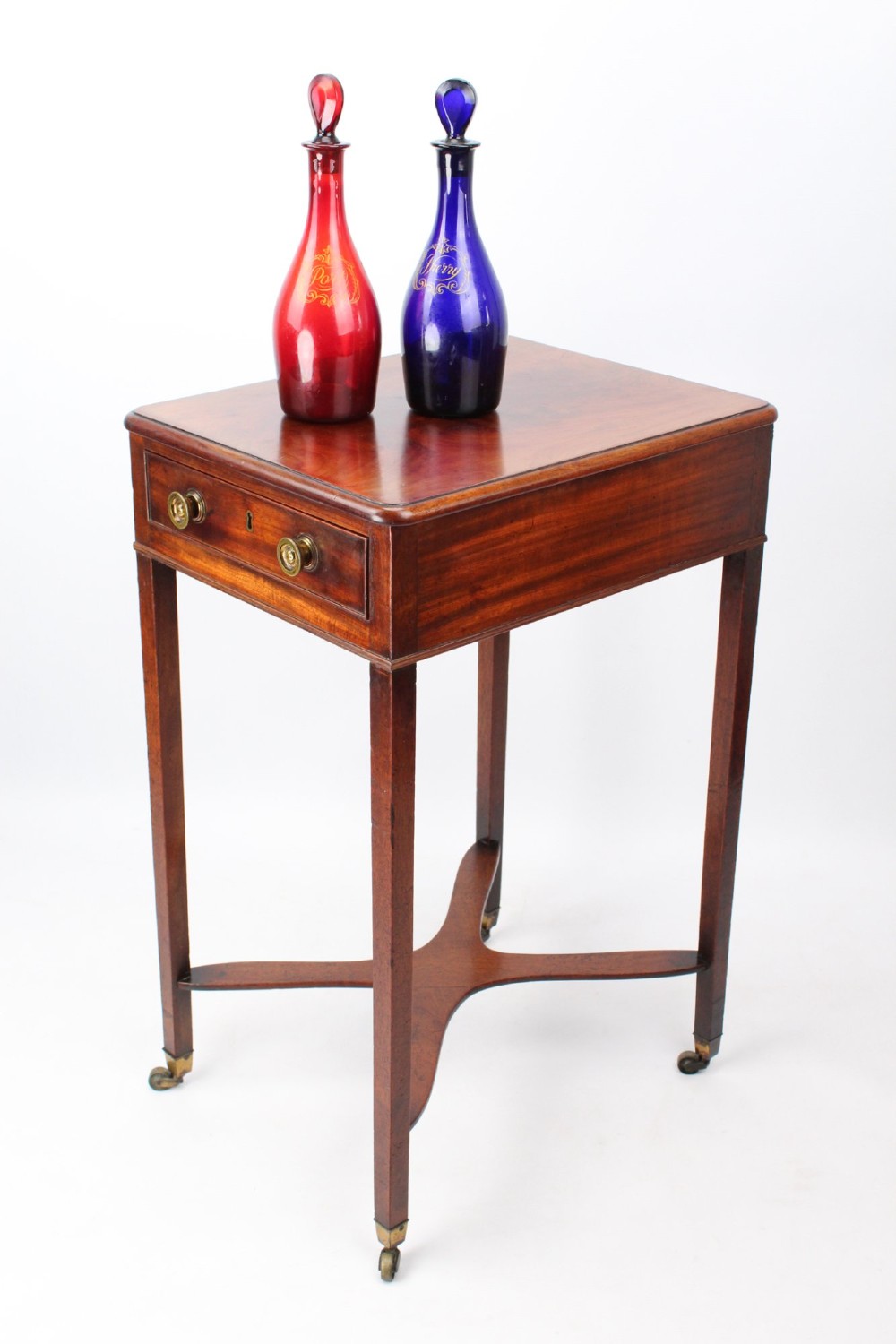 A small Georgian mahogany side table featuring a single drawer with brass ring handles, square tapered legs joined by an X-form stretcher, and brass castors. View VIII