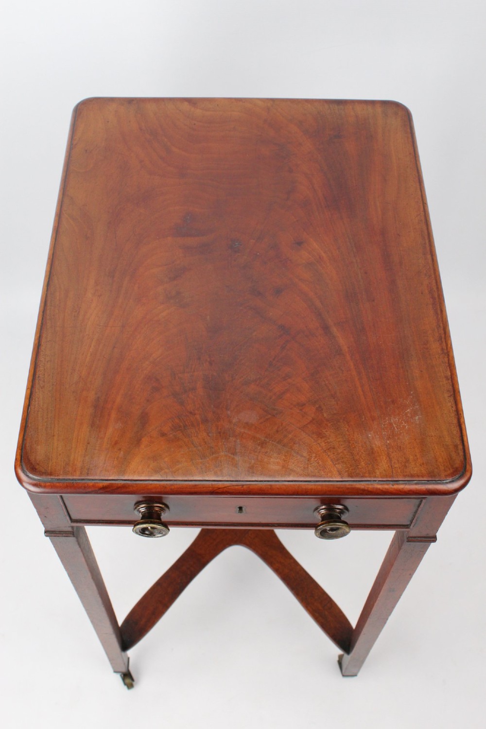 A small Georgian mahogany side table featuring a single drawer with brass ring handles, square tapered legs joined by an X-form stretcher, and brass castors. View IX