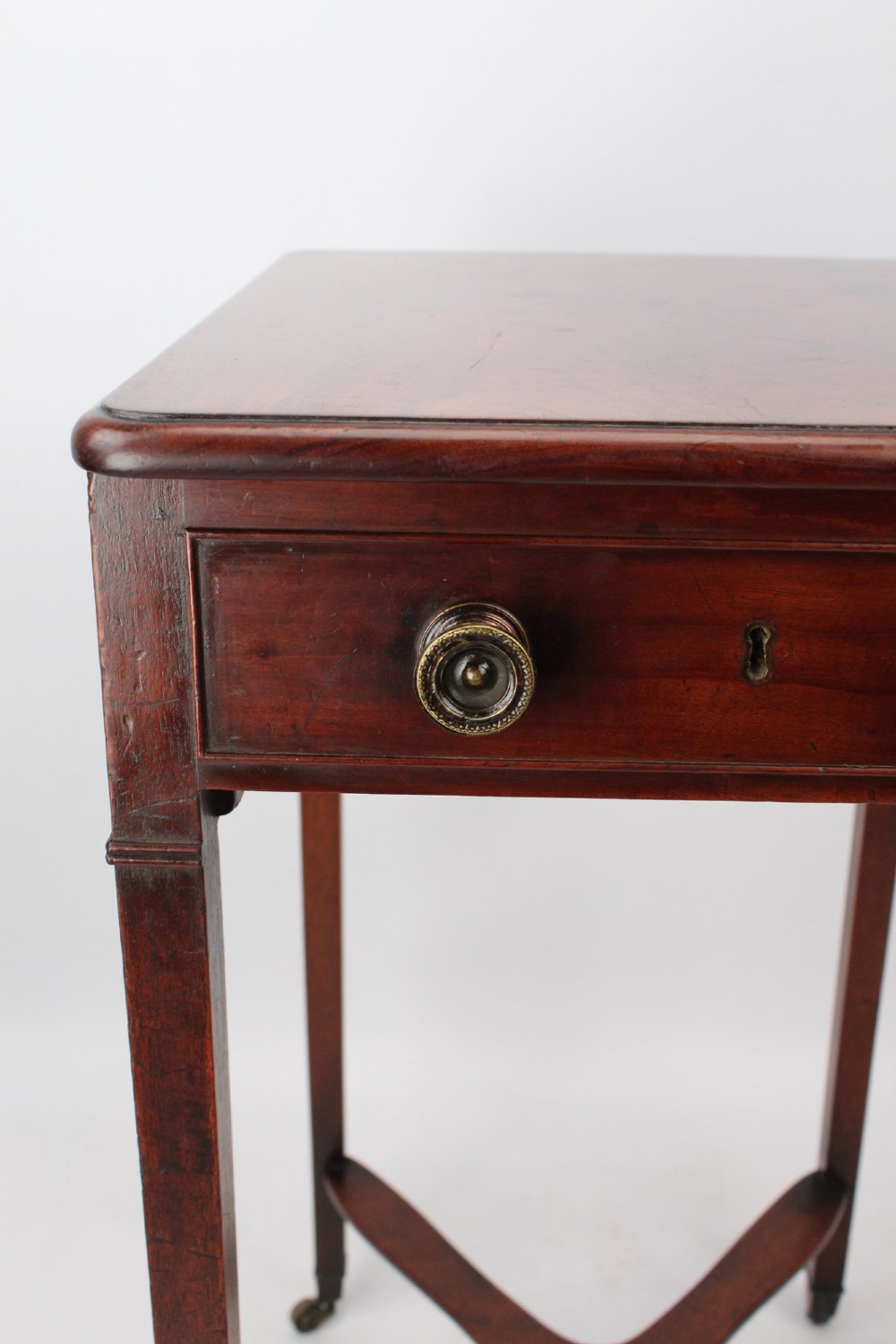 A small Georgian mahogany side table featuring a single drawer with brass ring handles, square tapered legs joined by an X-form stretcher, and brass castors. View X