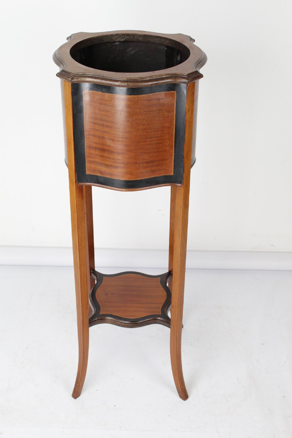 A tall Edwardian mahogany plant stand featuring shaped inlaid panels, four slender splayed legs, a lower shelf, and a dark metal liner. View II