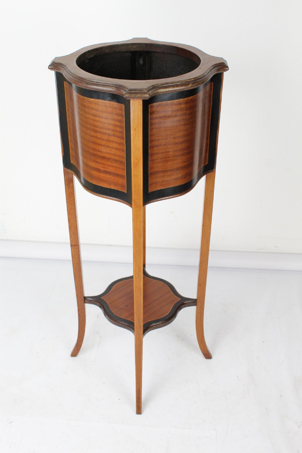 A tall Edwardian mahogany plant stand featuring shaped inlaid panels, four slender splayed legs, a lower shelf, and a dark metal liner. View III