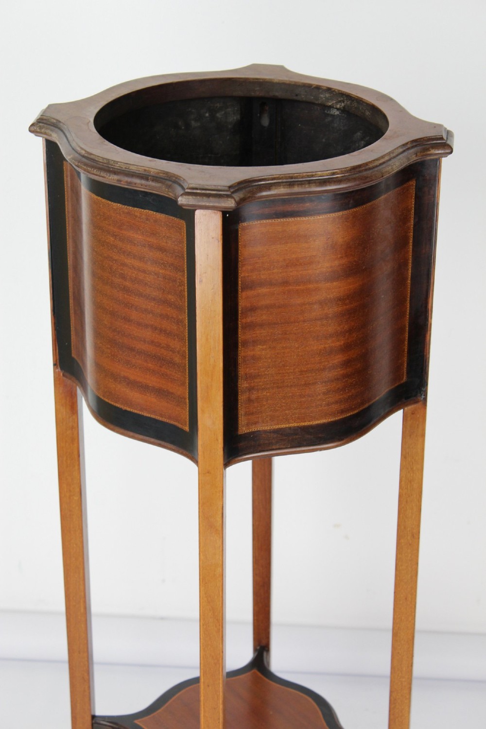 A tall Edwardian mahogany plant stand featuring shaped inlaid panels, four slender splayed legs, a lower shelf, and a dark metal liner. View IV