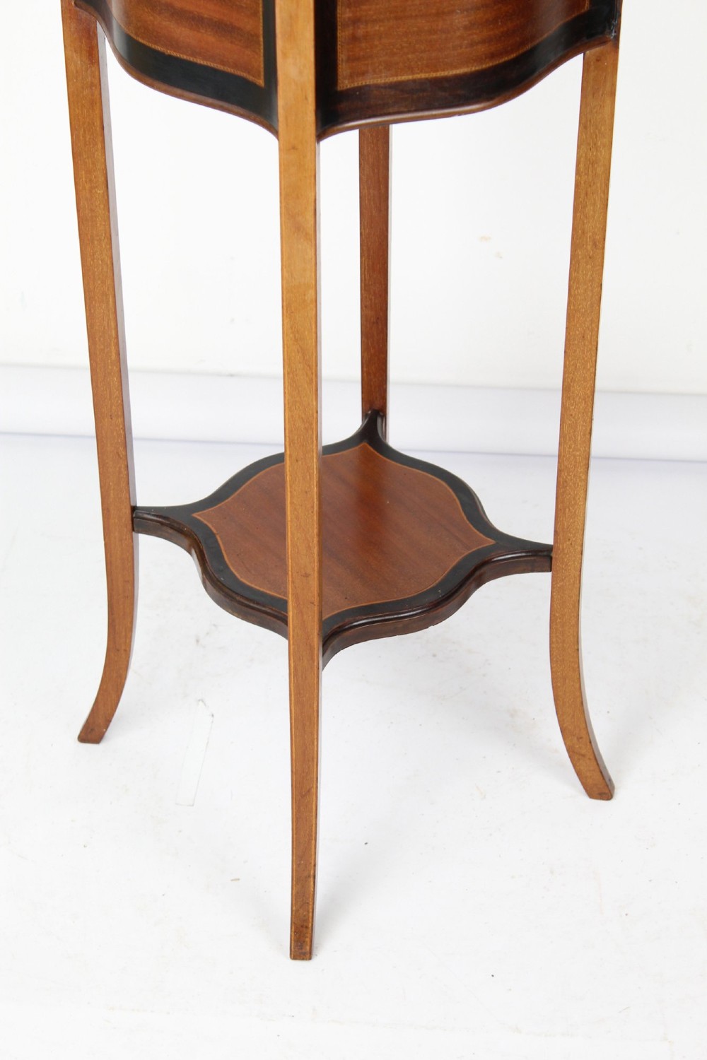 A tall Edwardian mahogany plant stand featuring shaped inlaid panels, four slender splayed legs, a lower shelf, and a dark metal liner. View V