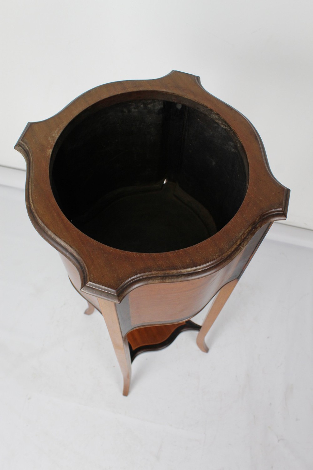 A tall Edwardian mahogany plant stand featuring shaped inlaid panels, four slender splayed legs, a lower shelf, and a dark metal liner. View VI