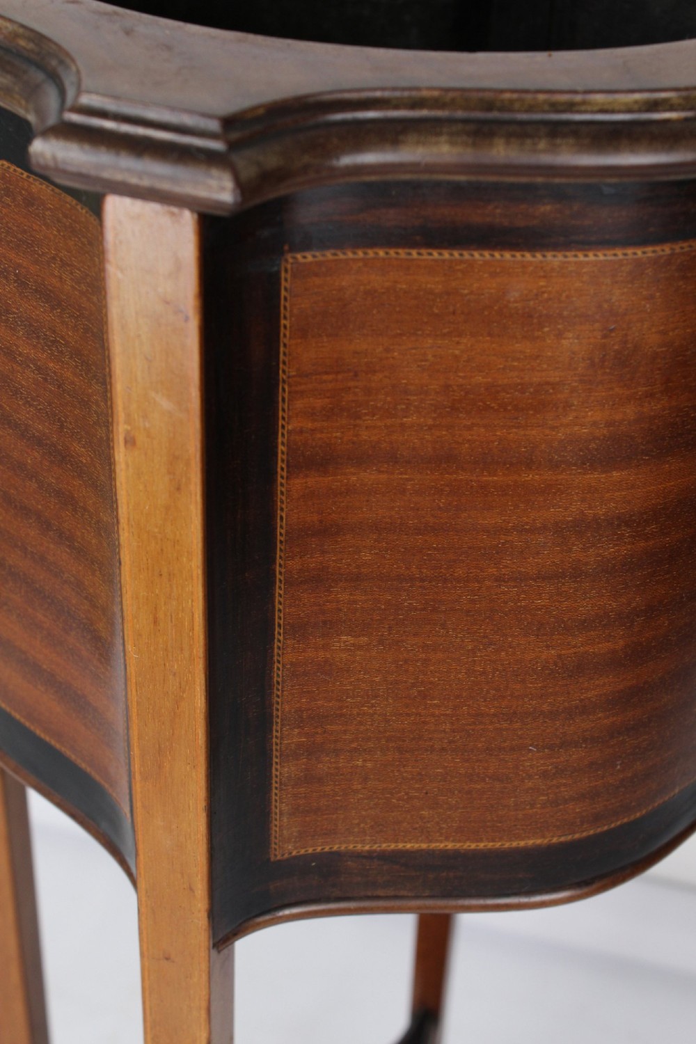 A tall Edwardian mahogany plant stand featuring shaped inlaid panels, four slender splayed legs, a lower shelf, and a dark metal liner. View VII