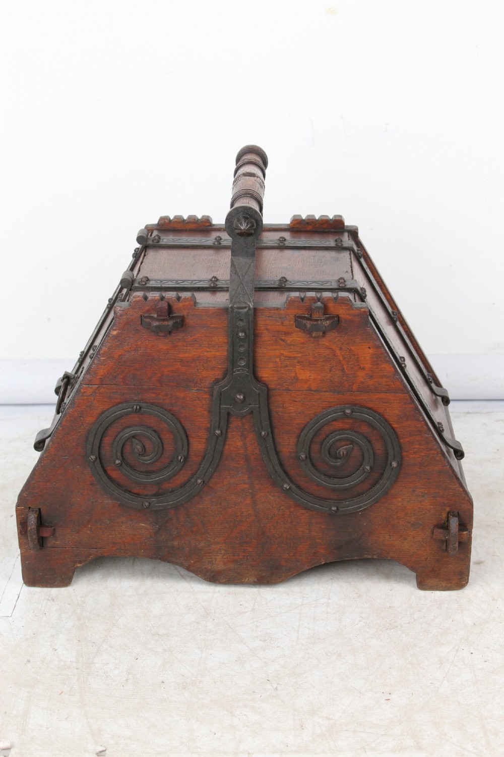 A Victorian Gothic Revival dark oak coal scuttle featuring sloped timber lids, a turned handle, and black wrought iron scrollwork straps. View V