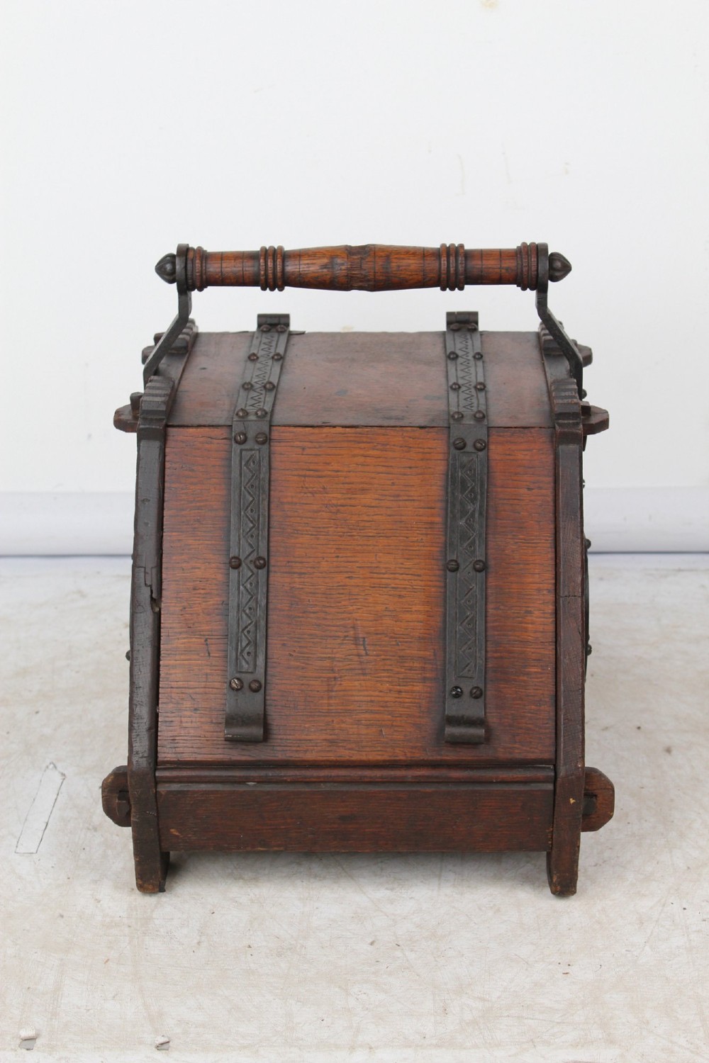 A Victorian Gothic Revival dark oak coal scuttle featuring sloped timber lids, a turned handle, and black wrought iron scrollwork straps. View VI