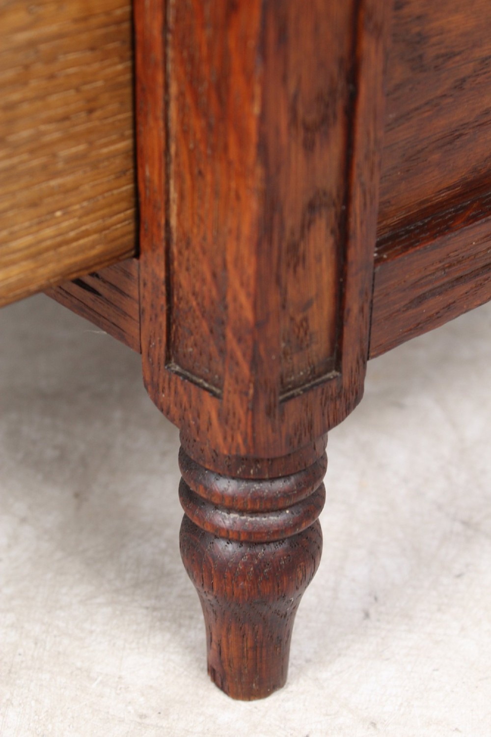 An Edwardian oak Canterbury with vertical panelled sides, internal dividers, a lower drawer with a brass handle, and corner finials. View VIII