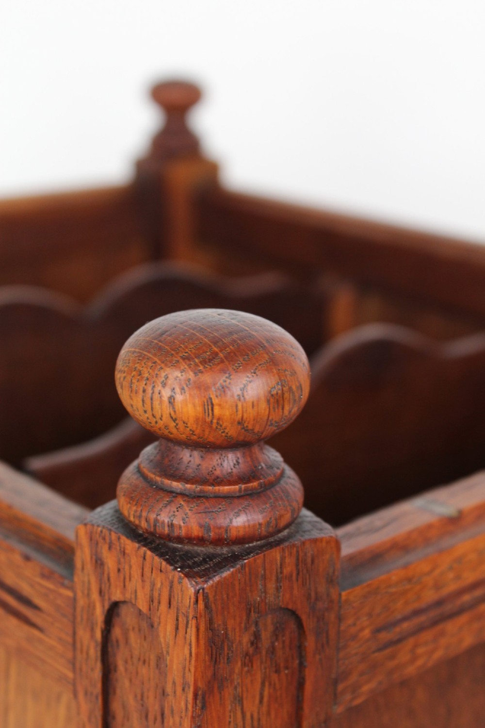 An Edwardian oak Canterbury with vertical panelled sides, internal dividers, a lower drawer with a brass handle, and corner finials. View IX