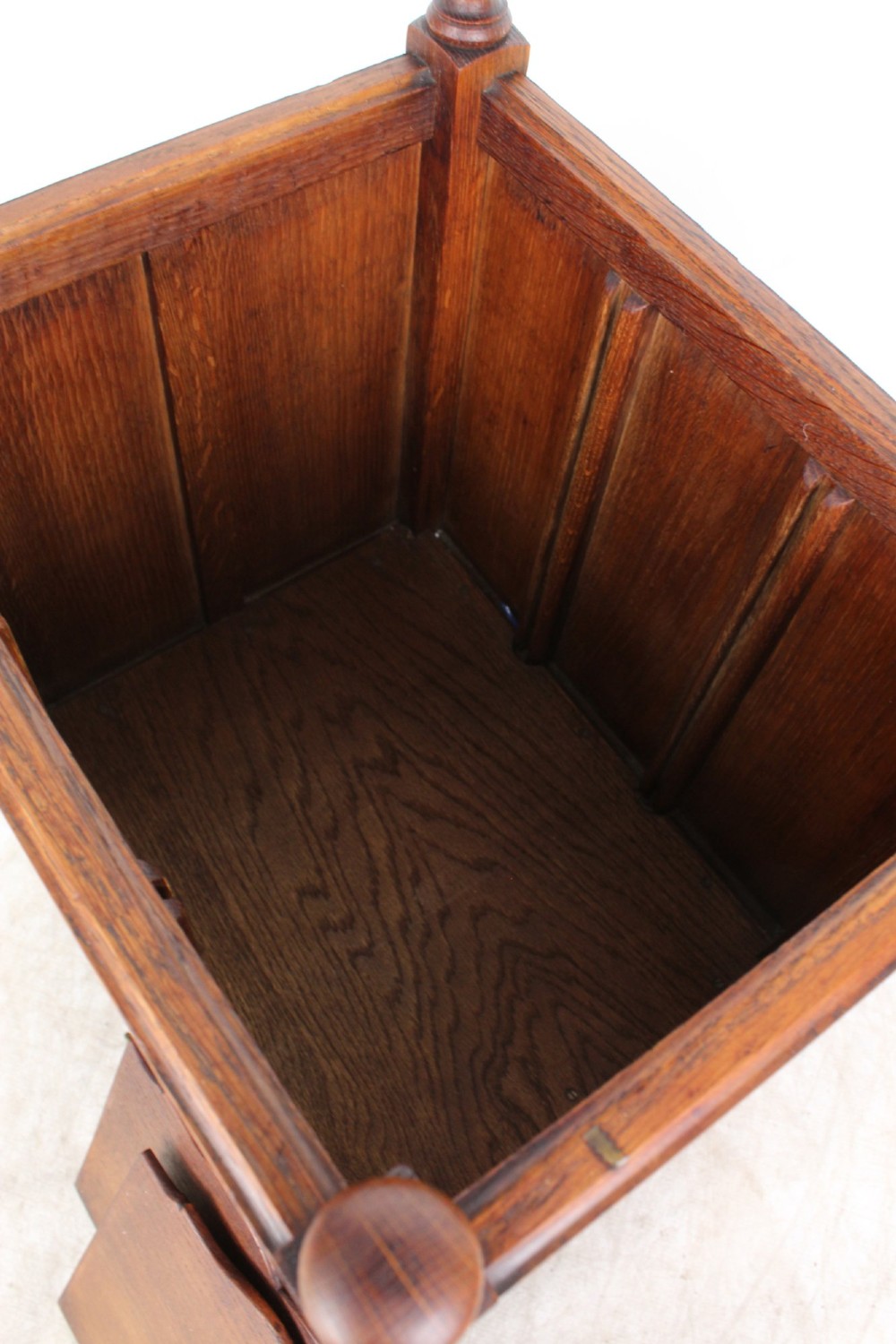 An Edwardian oak Canterbury with vertical panelled sides, internal dividers, a lower drawer with a brass handle, and corner finials. View XII