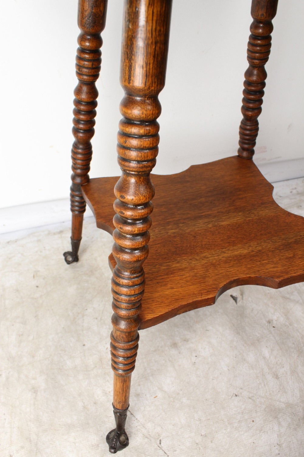 An antique warm brown oak side table featuring bobbin-turned legs, a lower rectangular shelf, and claw feet. View VII