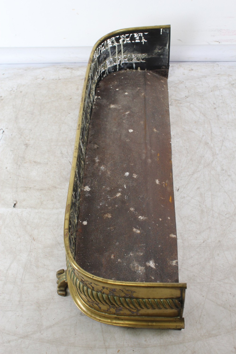 A low curved Victorian brass fire fender displaying a pierced fretwork panel, a central gadrooned band, and short cast scroll feet. View IV