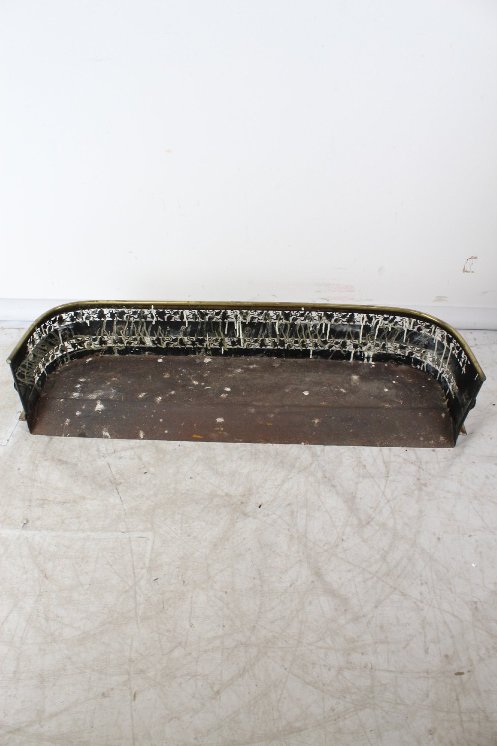 A low curved Victorian brass fire fender displaying a pierced fretwork panel, a central gadrooned band, and short cast scroll feet. View V