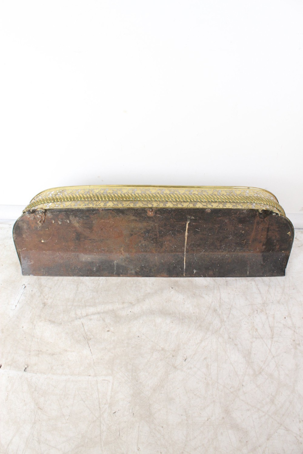 A low curved Victorian brass fire fender displaying a pierced fretwork panel, a central gadrooned band, and short cast scroll feet. View VI