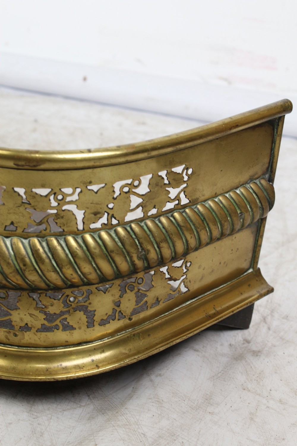 A low curved Victorian brass fire fender displaying a pierced fretwork panel, a central gadrooned band, and short cast scroll feet. View VII