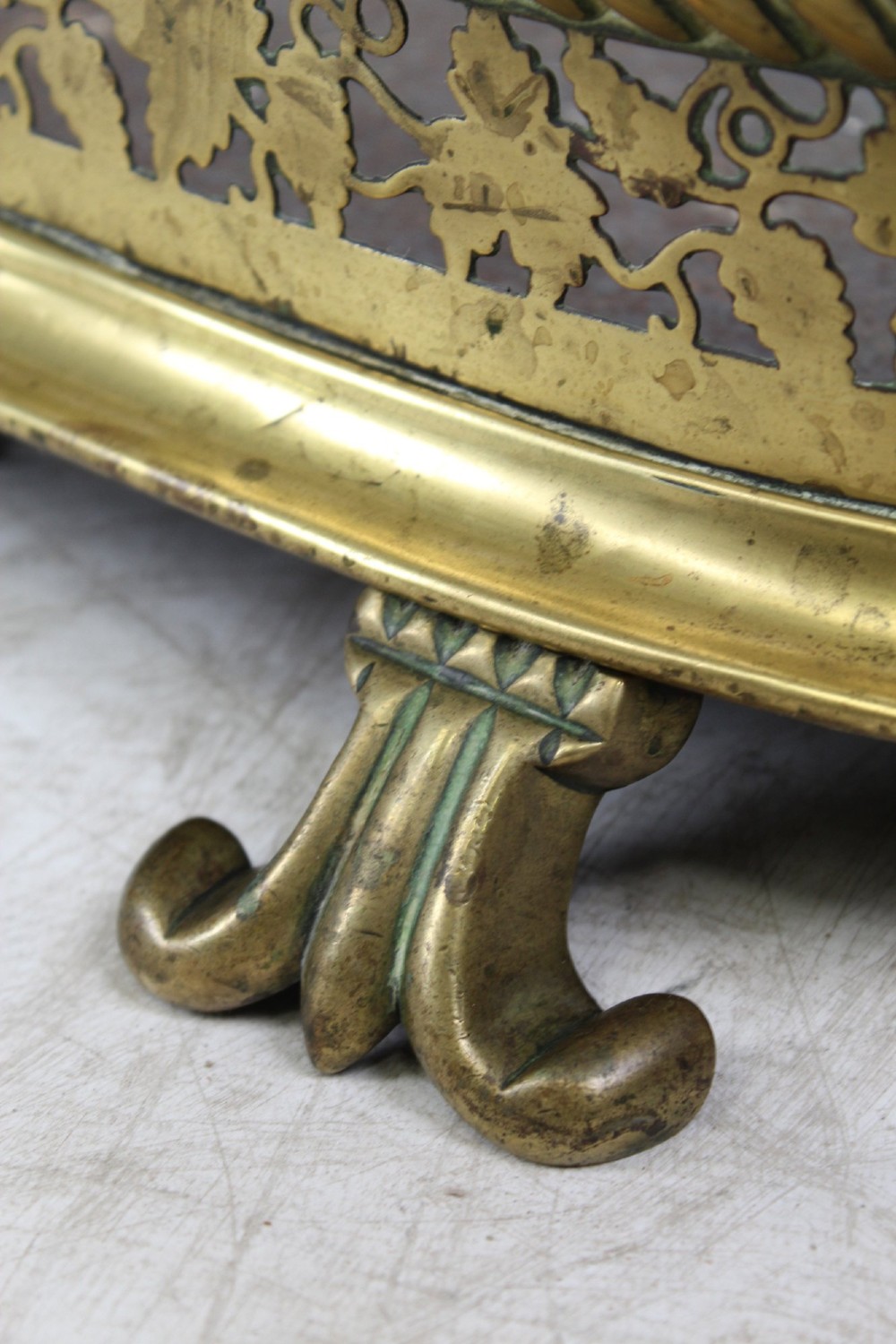 A low curved Victorian brass fire fender displaying a pierced fretwork panel, a central gadrooned band, and short cast scroll feet. View VIII