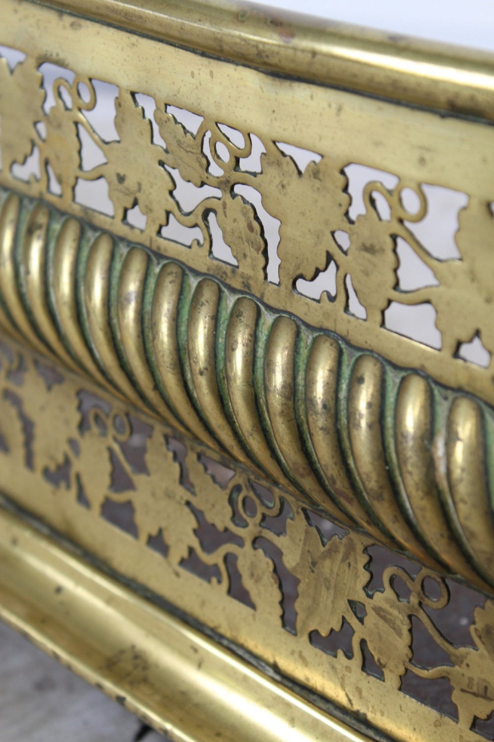 A low curved Victorian brass fire fender displaying a pierced fretwork panel, a central gadrooned band, and short cast scroll feet. View IX