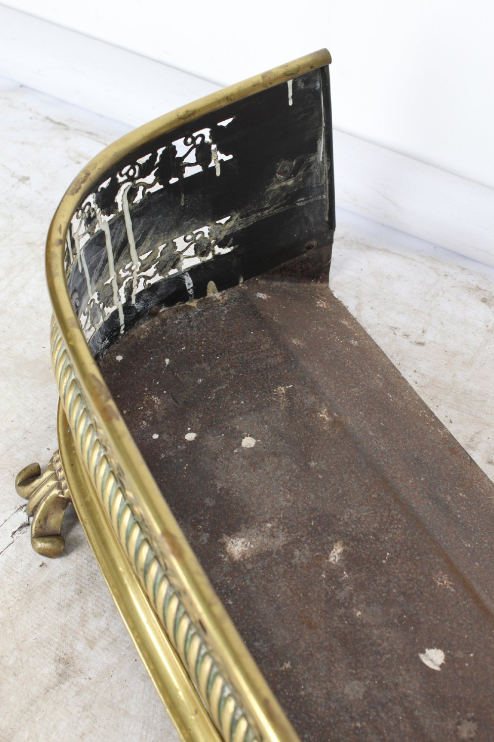 A low curved Victorian brass fire fender displaying a pierced fretwork panel, a central gadrooned band, and short cast scroll feet. View X