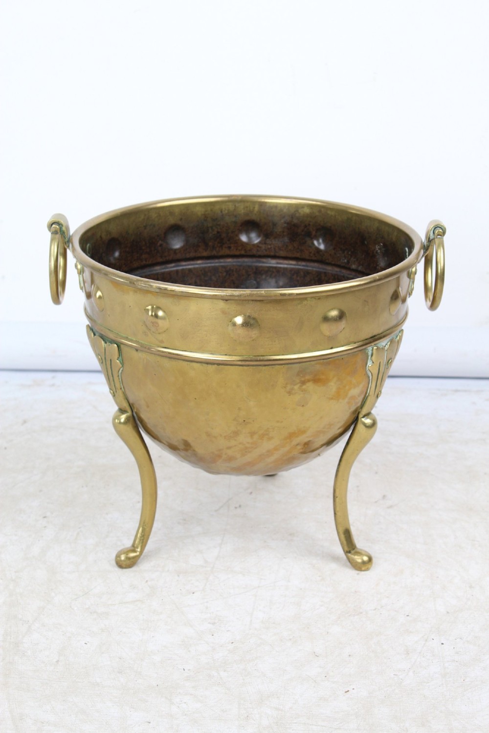 A Victorian Arts and Crafts brass log bin featuring raised round bosses around the rim, side drop rings, and curved legs.