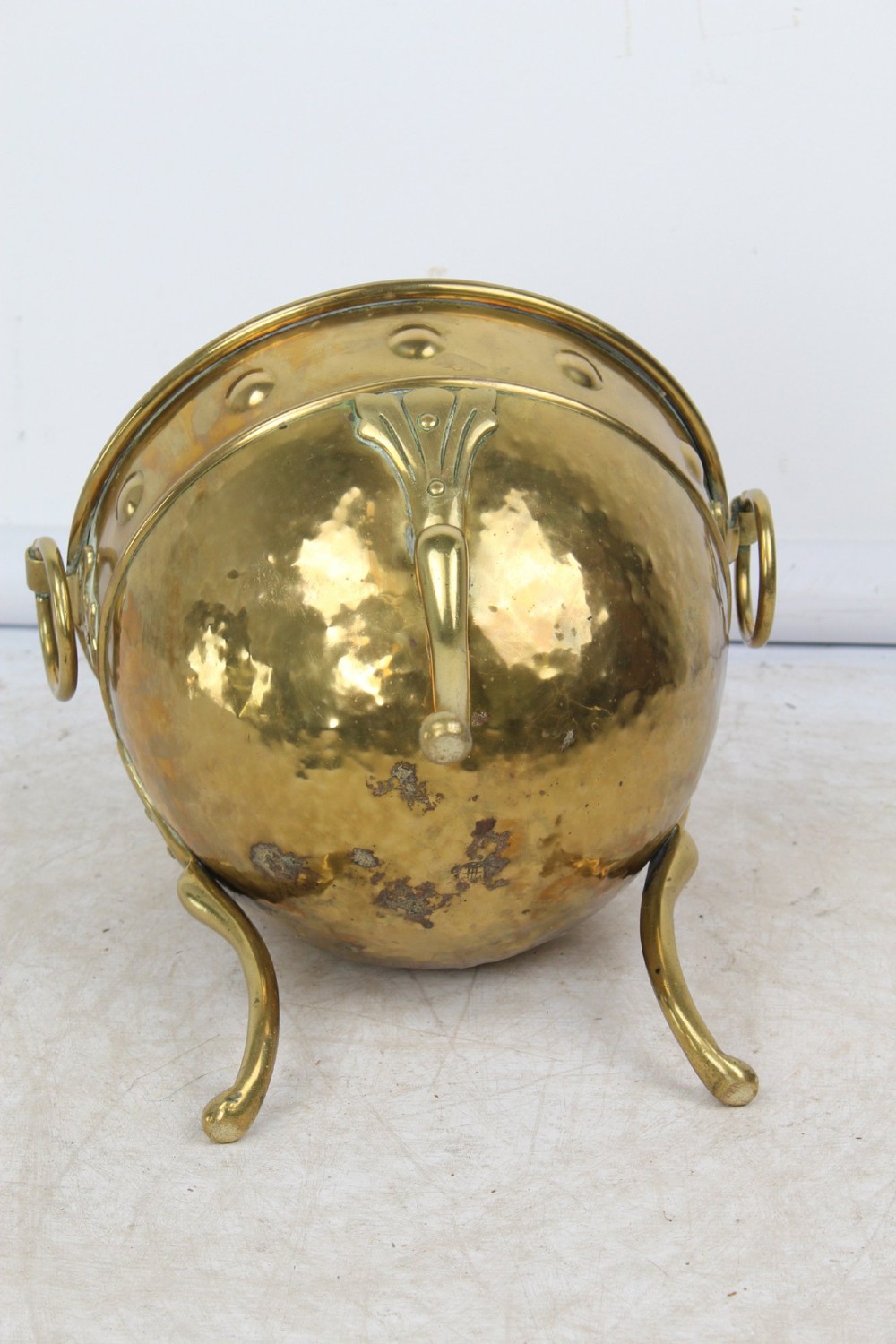 A Victorian Arts and Crafts brass log bin featuring raised round bosses around the rim, side drop rings, and curved legs. View V