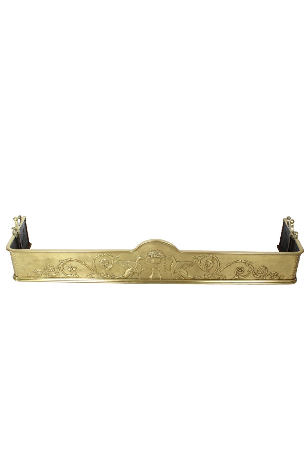 A long Victorian brass fireplace fender featuring embossed Neoclassical relief decoration of central urns, winged sphinxes, and foliate scrolls.