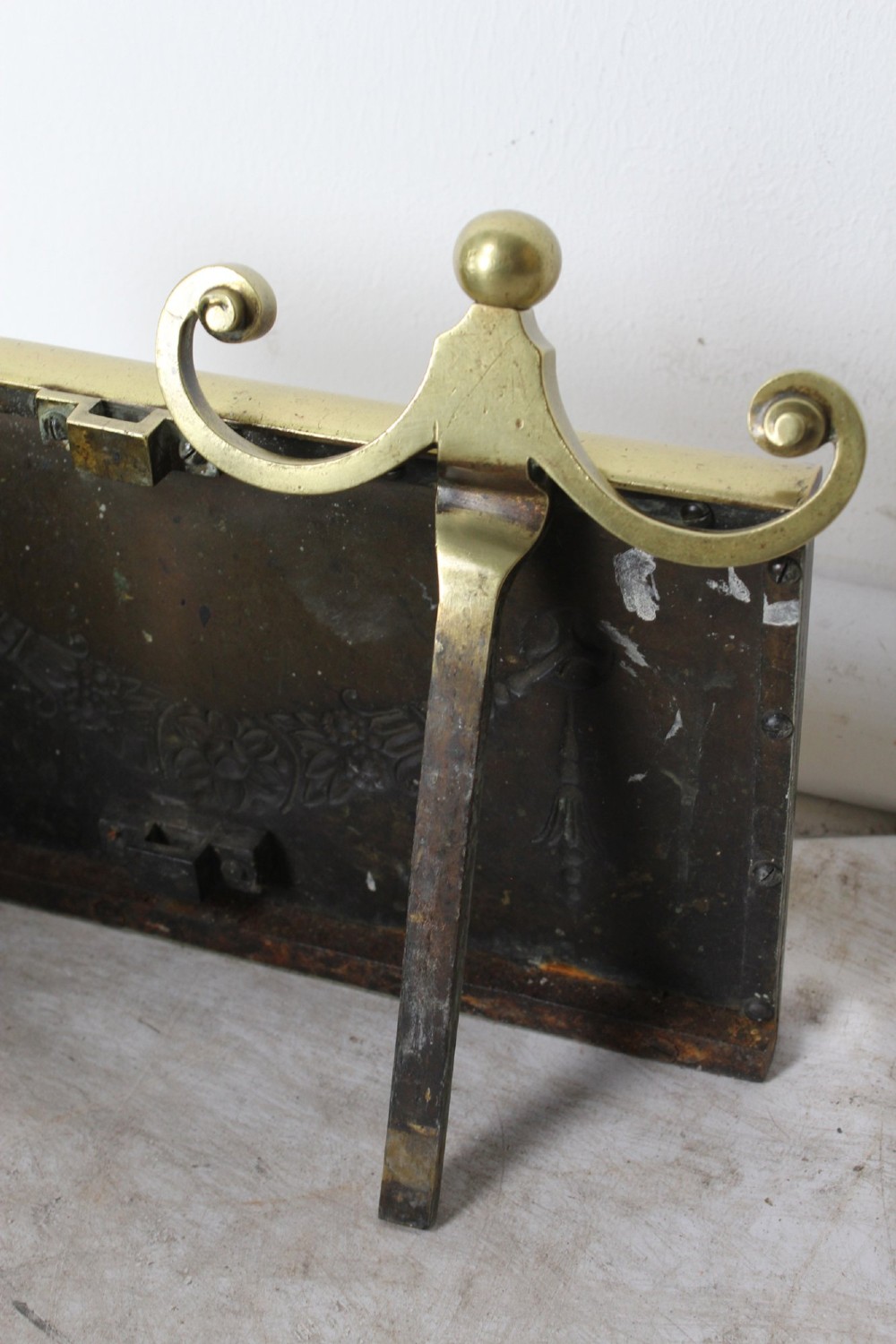 A long Victorian brass fireplace fender featuring embossed Neoclassical relief decoration of central urns, winged sphinxes, and foliate scrolls. View IX