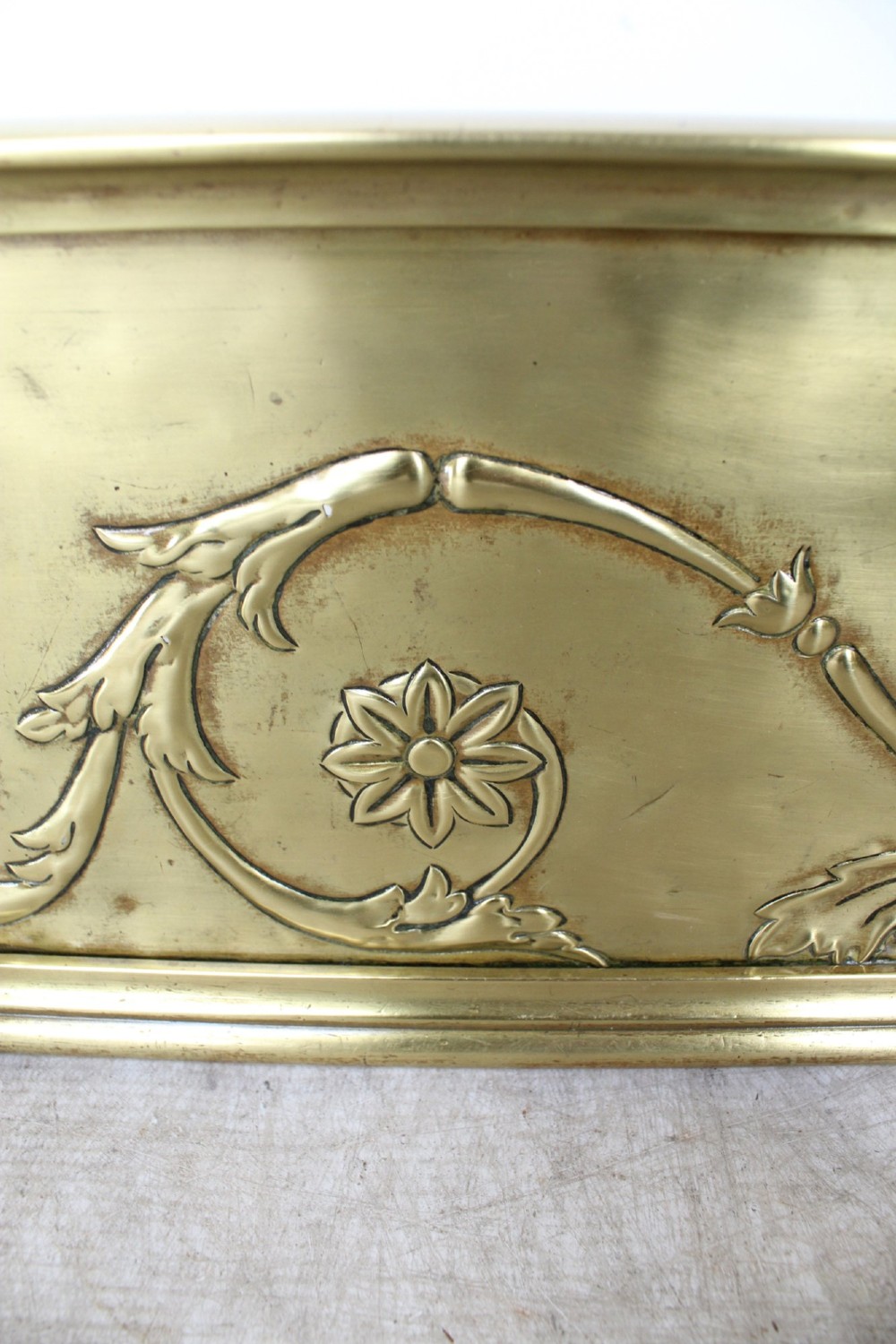 A long Victorian brass fireplace fender featuring embossed Neoclassical relief decoration of central urns, winged sphinxes, and foliate scrolls. View XII
