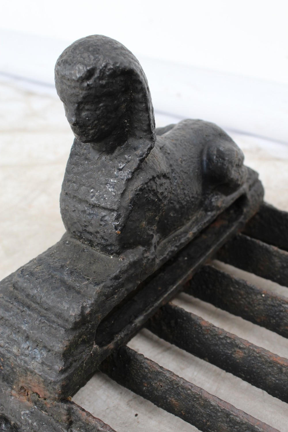 A dark cast iron boot scraper featuring twin sphinx figures flanking a central slatted grate set upon a decorative moulded base. View VII